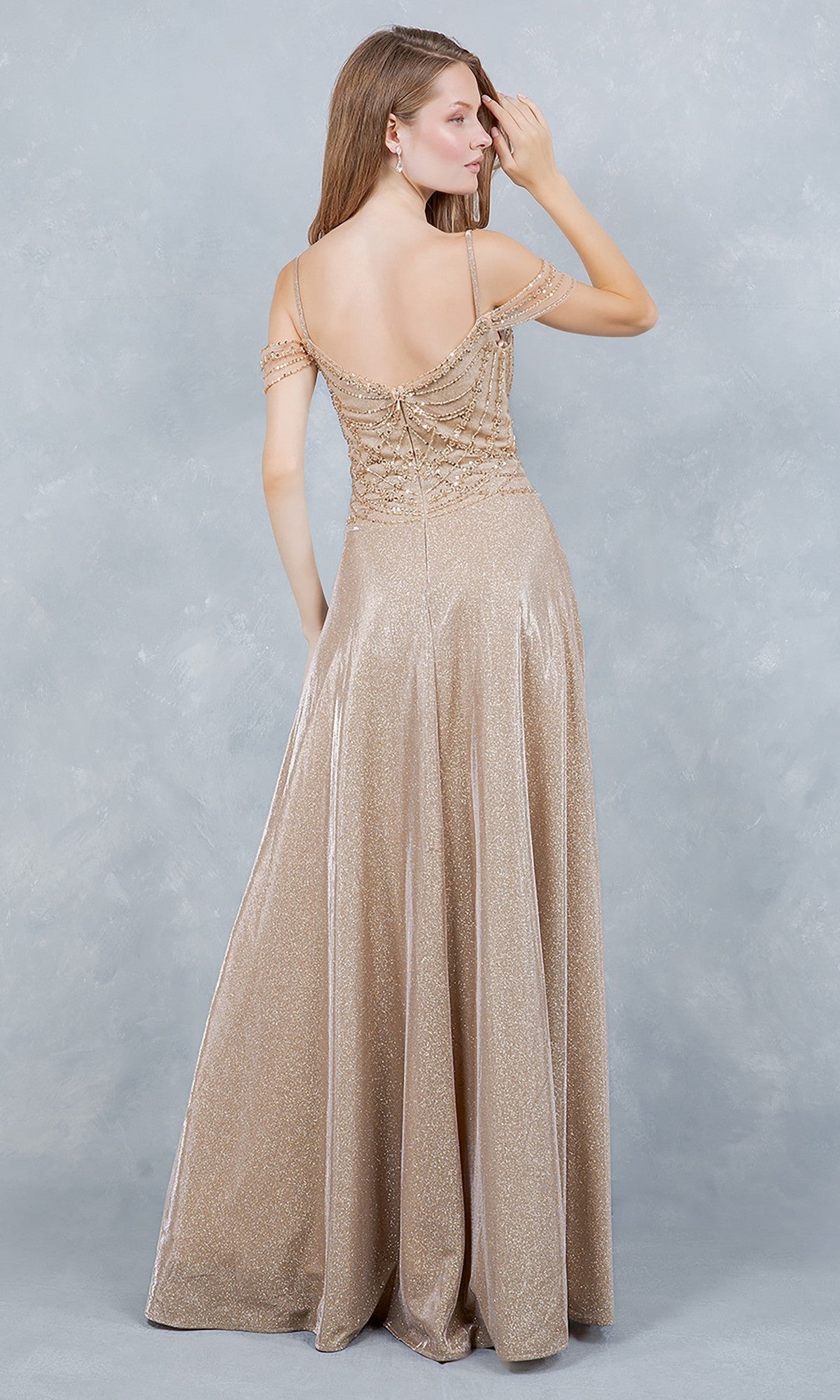 A woman faces away in the Cinderella Couture 8581J—an off-the-shoulder glitter prom dress with a beaded bodice, thin straps, and a floor-length A-line skirt—set against a light gray textured background.
